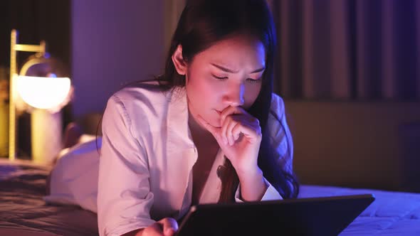 Young Asian beautiful woman enjoy using smartphone- tablet   in bedroom at night time.