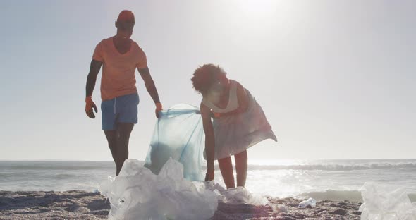 African american couple segregating waste with gloves on sunny beach