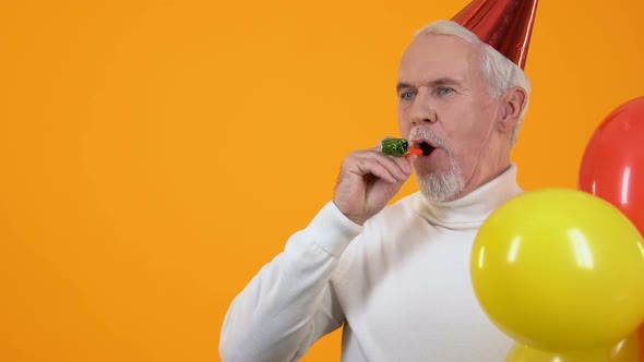 Cheerful Aged Man Blowing Party Horn Holding Colorful Balloons, Event Greeting