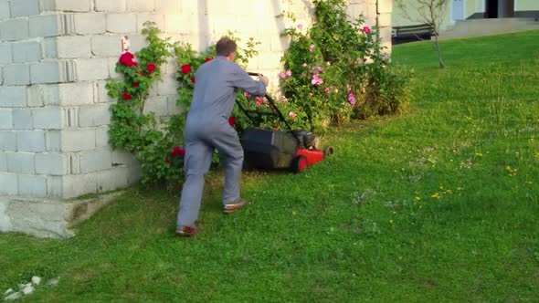 Man trimming his lawn around his garage with petrol rotary lawn mower machine.