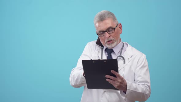 Adult doctor speaks on the phone and writes on a paper tablet, looking at a wristwatch in blue