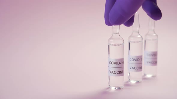 Coronavirus vaccine. A hand in blue protective medical gloves picks up an ampoule among others 