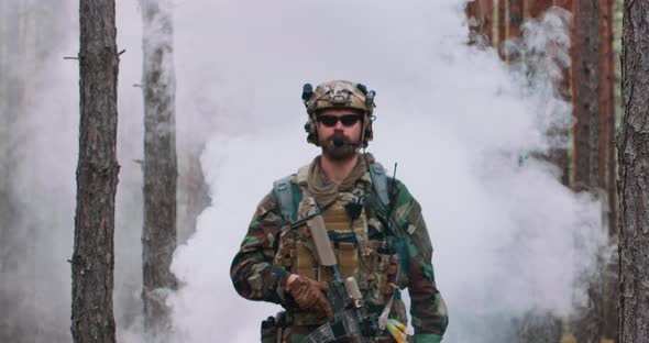 Fully Equipped Soldier in a Camouflage Uniform Emerging From a Puff of Smoke in the Middle of a Pine
