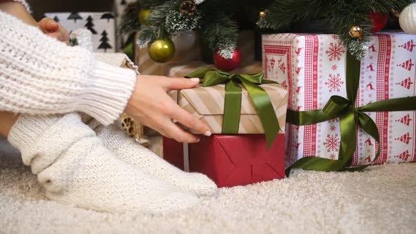 Female Legs In Socks Sitting Near Christmas Tree With Gift Boxes