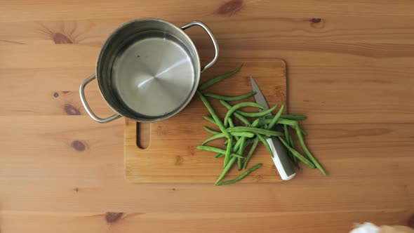 Top down view of hands emptying a bag of green beans and cutting them on a bamboo cutting board, and