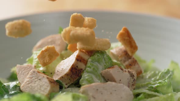 Camera follows putting croutons over salad with grilled chicken. Slow Motion.