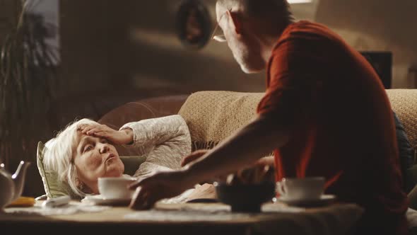 Senior Man Measuring Temperature and Giving Tea to Woman