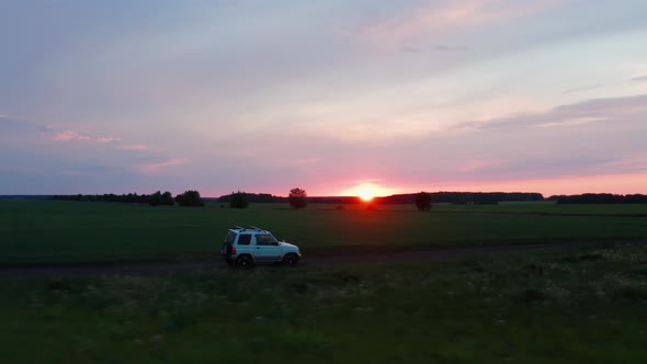 Aerial View of a Car Driving in Nature on a Field at Sunset