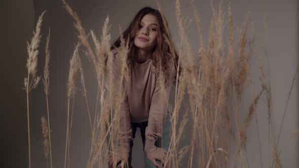 Beautiful European Girl with Flowing Hair in Stylish Clothes Behind Ears of Wheat Looks at Camera