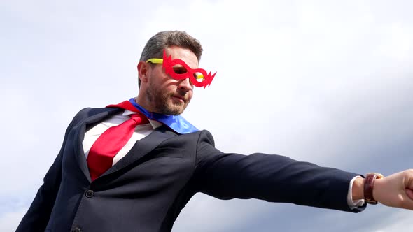 Businessman in Superhero Suit with Raised Hand on Sky Background Business Success