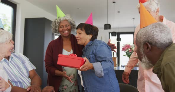 Happy senior diverse people at birthday party with cake and gifts at retirement home