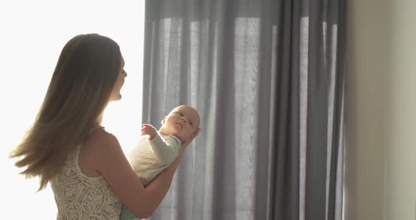 Happy Mother Holds Lovely Newborn Son Plays with Him and Turns Around in Room