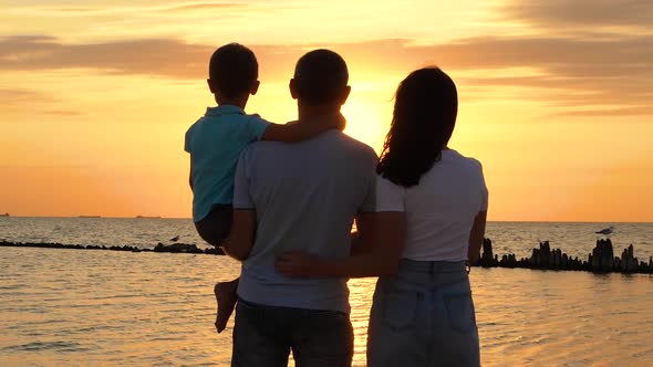 A Happy Family Enjoys a Beautiful Sunset Standing on the Seashore. A Woman Embraces a Man. Family