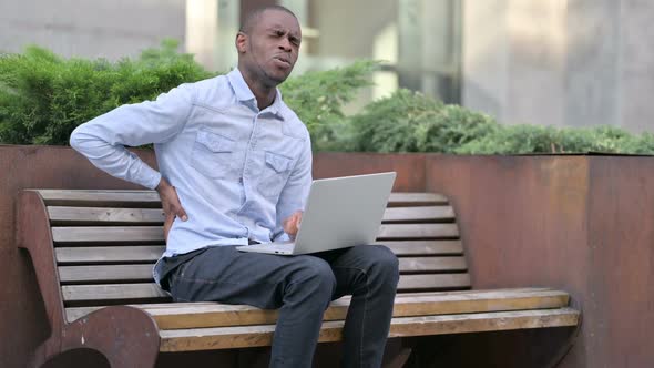 African Man with Back Pain Using Laptop Outdoor