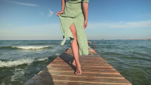 Slow Motion Woman in a Dress in the Wind Walks Along the Pier on the Seashore on a Sunny Day