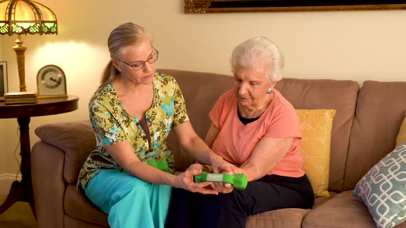 Home healthcare therapist helping elderly woman with physical therapy with hand weights.