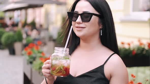 Attractive Young Woman in Sunglasses Is Drinking a Cocktail in the Summer City