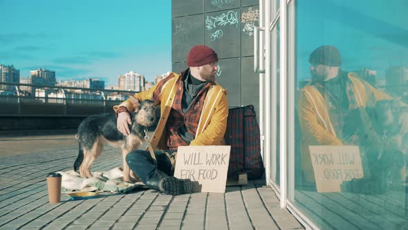 A Homeless Man is Sitting on the Street and Petting a Dog