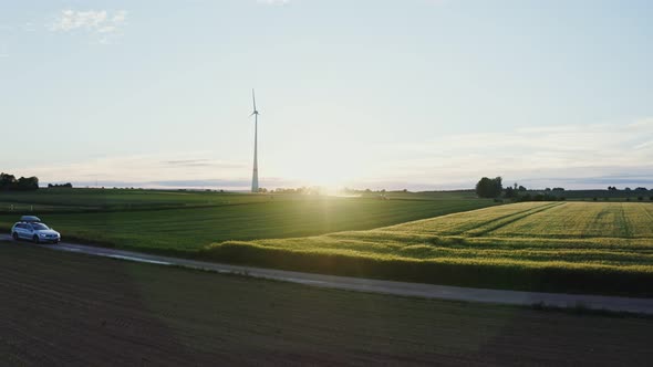 The Light of the Rising Sun Illuminates the Meadow on Which is Wind Generator