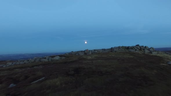 Aerial shot of men climbing boulders while bouldering at night under a full moon.