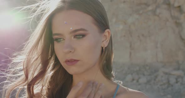 Beautiful Woman Corrects Blowing Hair and Looks at Camera Thoughtfully at Cliffs