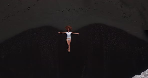 Aerial View of a Woman, Lying on the Beach with Black Sand