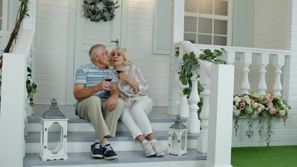 Attractive Senior Elderly Caucasian Couple Sitting and Drinking Wine in Porch at Home, Making a Kiss