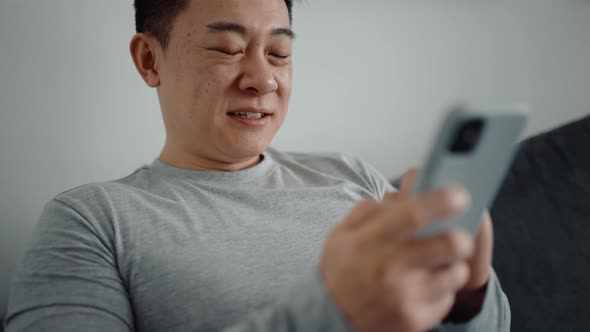 Laughing Asian man texting by phone