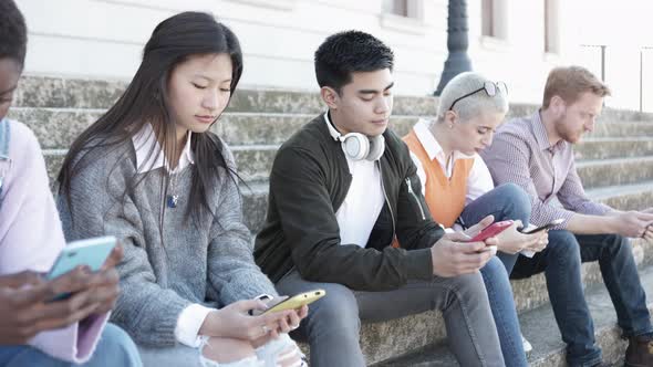 Multiethnic Young People Relaxing with Smartphones Sitting Outdoors