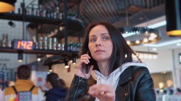 A Brunette Woman of Caucasian Nationality in a White Sweater and Black Jacket Sits in a Cozy Cafe