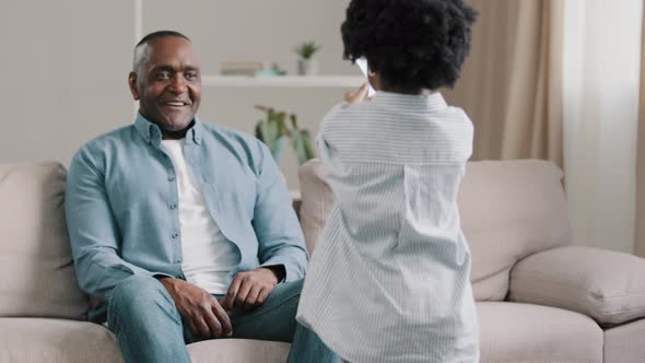 African American Man Sitting on Sofa in Room Accepting Congratulations Caring Daughter Gives Card to