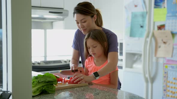 Mother teaching daughter to chop vegetables in kitchen 