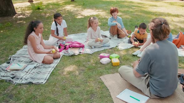 Teacher and Schoolchildren Talking and Relaxing in Park