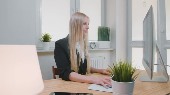 Smiling Woman Working on Computer in Office. Beautiful Young Blond Female Sitting at Workplace with
