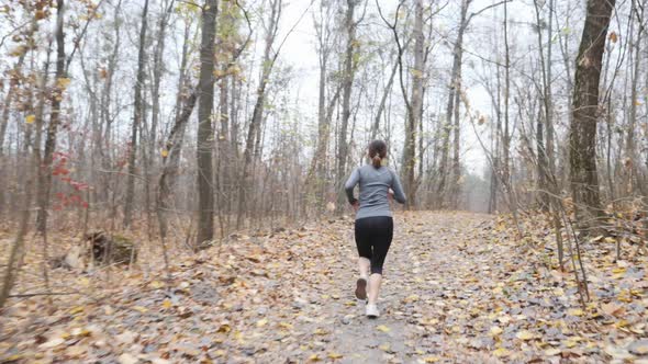 Chubby woman running in the park preparing for marathon wearing black and grey sports clothes