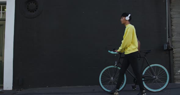 Transgender adult walking with a bike and using headphones