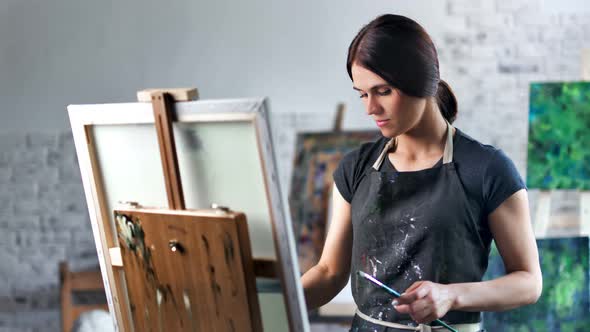 Happy Concentrated Beautiful Female Painter Enjoying Drawing Picture in Art Studio Medium Shot