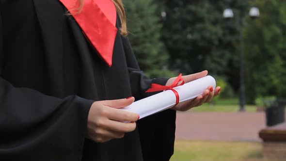 Young Woman in Academic Dress Holding Diploma, Enjoying Graduation Ceremony