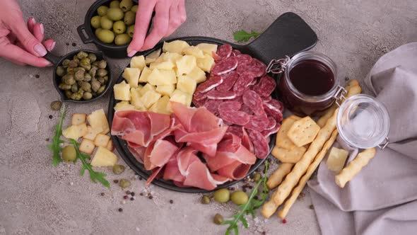 Making Meat and Cheese Antipasto Plater Woman Adding Capers and Olives to Serving Board with Cheese