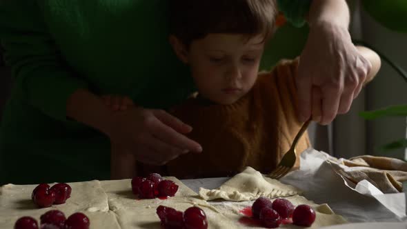 Mother with a son cooking cookies with a cherry at home.