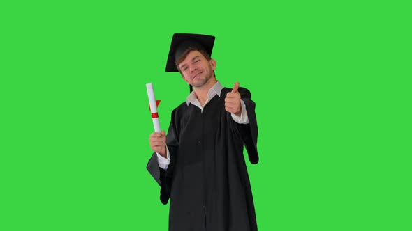 Happy Male Student in Graduation Robe Posing with His Diploma and Showing Thumbs Up on a Green