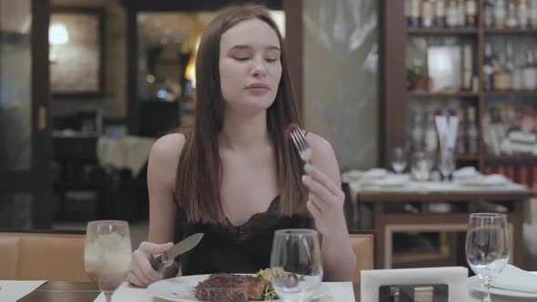 Portrait of Young Woman Cutting Tasty Steak Lying with Vegetables and Leaves on the Plate