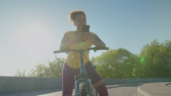 Lovely Black Woman on Bicycle Networking on Cellphone at Dawn