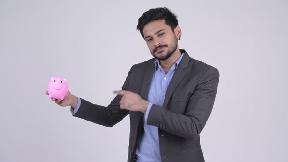 Young Happy Bearded Indian Businessman Holding Piggy Bank and Giving Thumbs Up