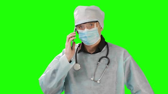 Young Doctor in Medical Mask and Protective Medical Clothing Talking on the Phone. Shot on the