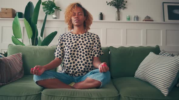 Calm Young Dark Skinned Woman Meditating at Home While Sitting on Sofa