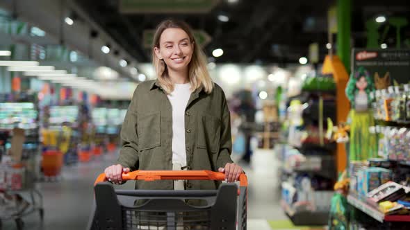 young happy woman pushing trolley spends time in a supermarket or mall store.