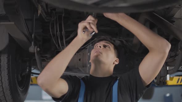 Portrait of Professional Repairman Tightening Screws Under Car in Repair Shop