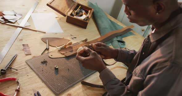 Focused african american craftsman using tools to make a belt in leather workshop