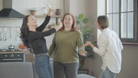 Three Cheerful Women Dancing in Kitchen at Home